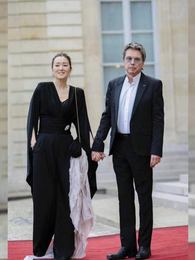 总统夫妇那边是老婆主动去挽老公的手,而巩俐这边,老公更主动去牵她