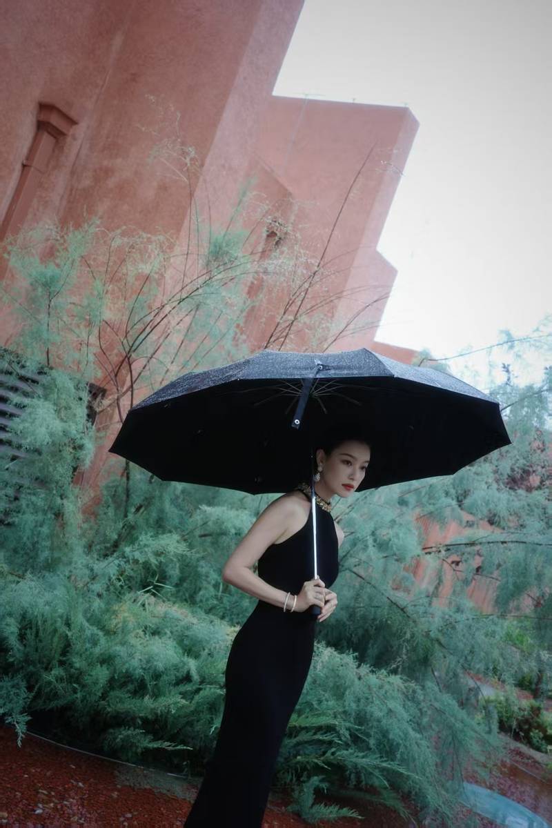 倪妮穿挂脖裙身材曼妙 撑黑伞漫步雨中尽显故事感