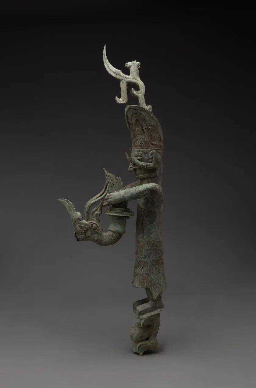 商 青铜持龙立人像三星堆博物馆藏辫发立人头戴高冠,耳插獐牙,身着